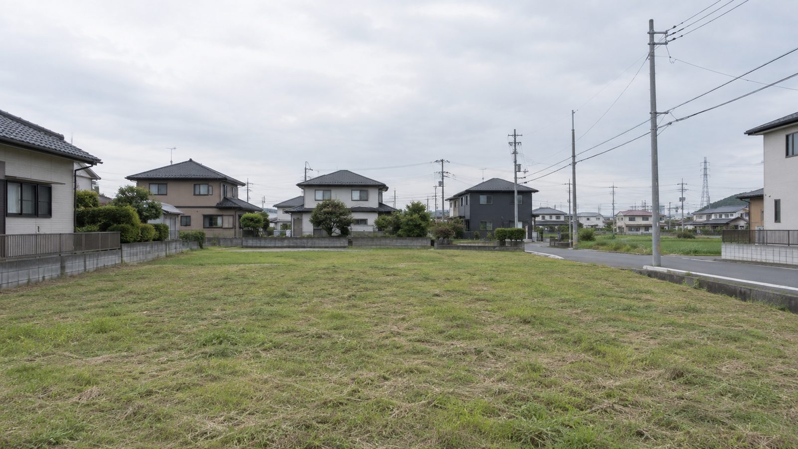 一宮市周辺の郊外にある、草を短く刈った更地。奥に住宅街が見える