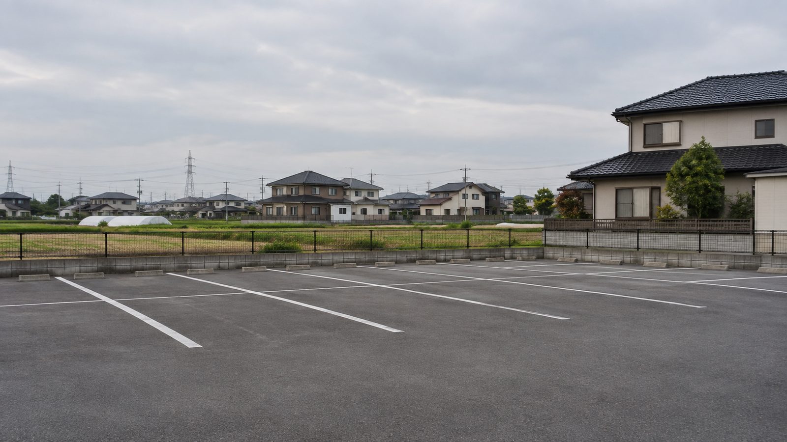 白線で区画が引かれた月極駐車場。奥に住宅とフェンス